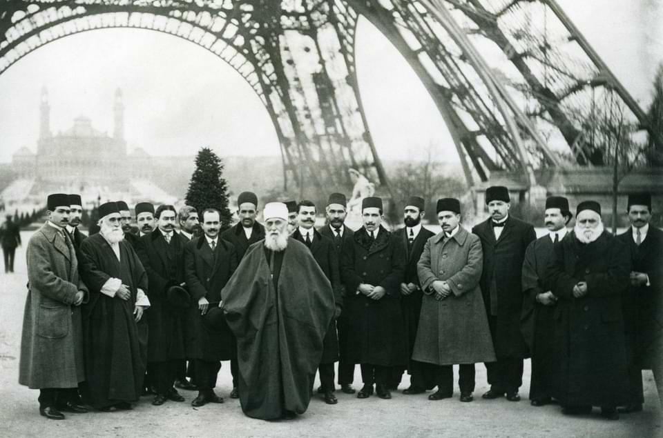 Ιστορική ασπρόμαυρη φωτογραφία του Αμπντούλ-Μπαχά με ομάδα ανδρών στο Παρίσι, με φόντο τον Πύργο του Άιφελ.