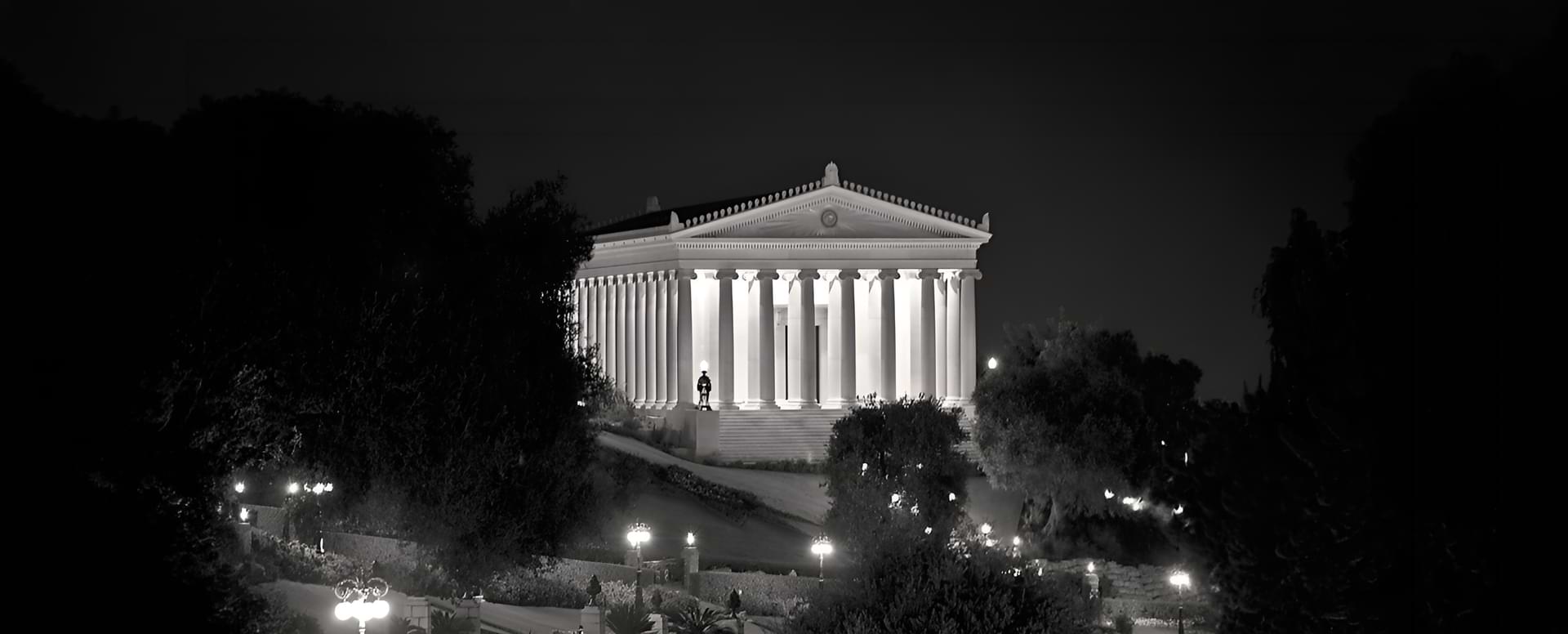 Νυχτερινή ασπρόμαυρη λήψη του Κτιρίου του Διεθνούς Αρχείου με την κλασική ελληνική αρχιτεκτονική και τους φωτισμένους κίονες.