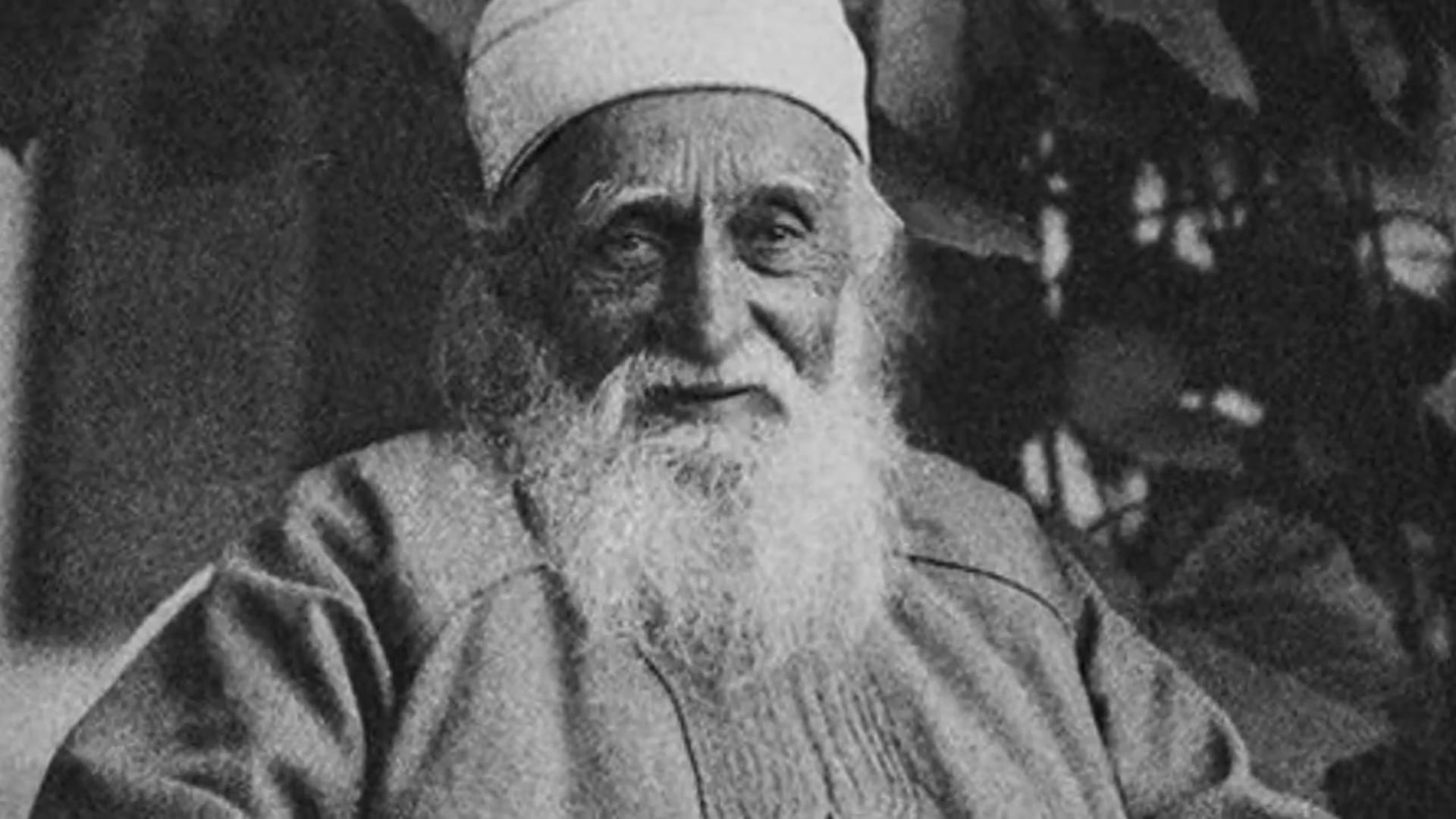 Ασπρόμαυρη φωτογραφία του Αμπντούλ-Μπαχά σε προχωρημένη ηλικία, με λευκή γενειάδα και παραδοσιακό κάλυμμα κεφαλής (ταρμπούς), σε κοντινό πλάνο